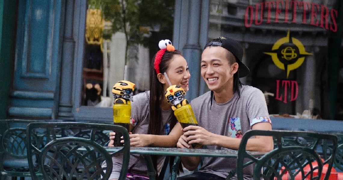 A cheerful scene from the film "Lion Men" shows two characters holding yellow toys outside a store, smiling and enjoying each other's company.