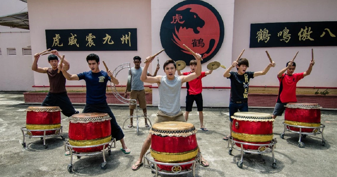 A group of performers practice drumming in front of a mural in a scene from the Singaporean film "Lion Men."