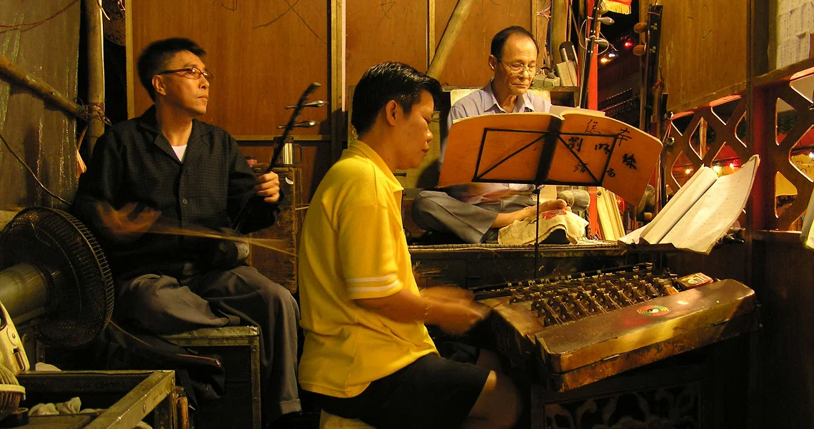 Musicians perform in a dimly lit setting for the Singaporean film "The Maid", showcasing traditional instruments and a keyboard.