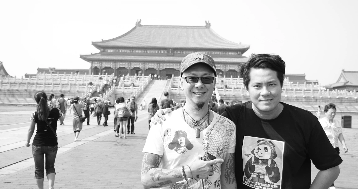 Two men stand in front of a traditional Chinese palace in "The Naked DJ" film still, showcasing architectural grandeur.