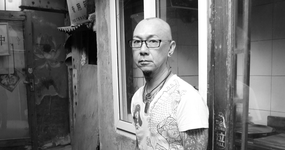 A bald man with glasses stands in a doorway, looking thoughtfully to the side in a film still from "The Naked DJ".