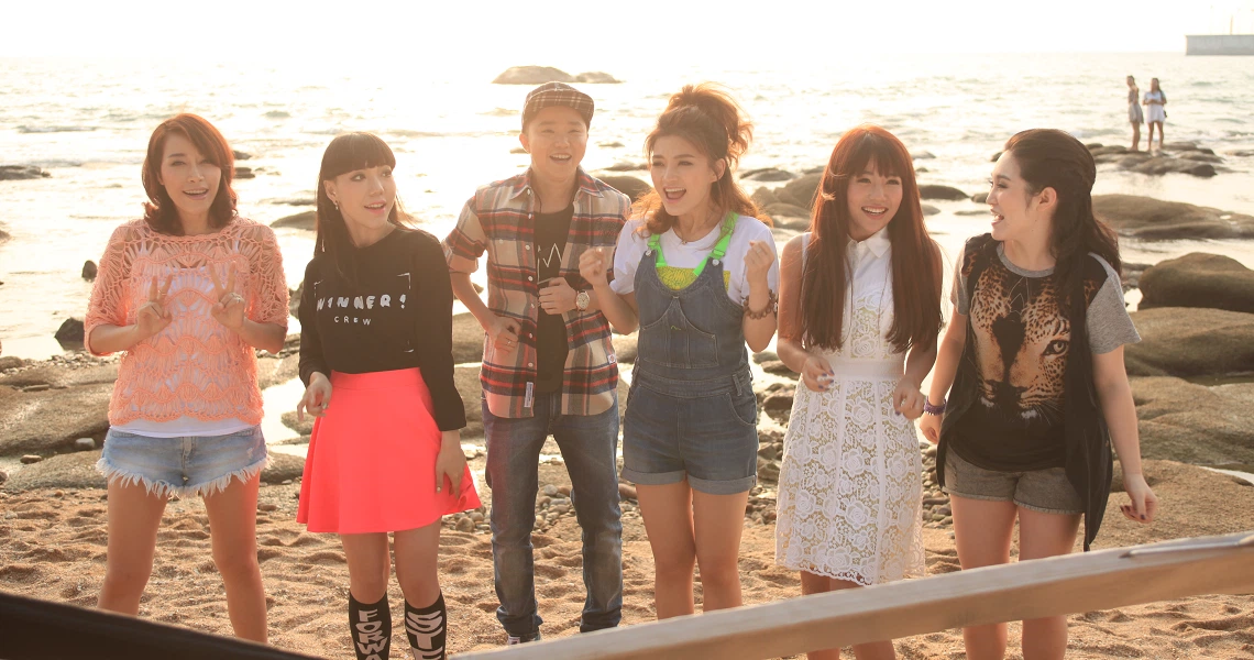 Film still from "Turn You Around" showing a group of young people standing together on a beach at sunset.