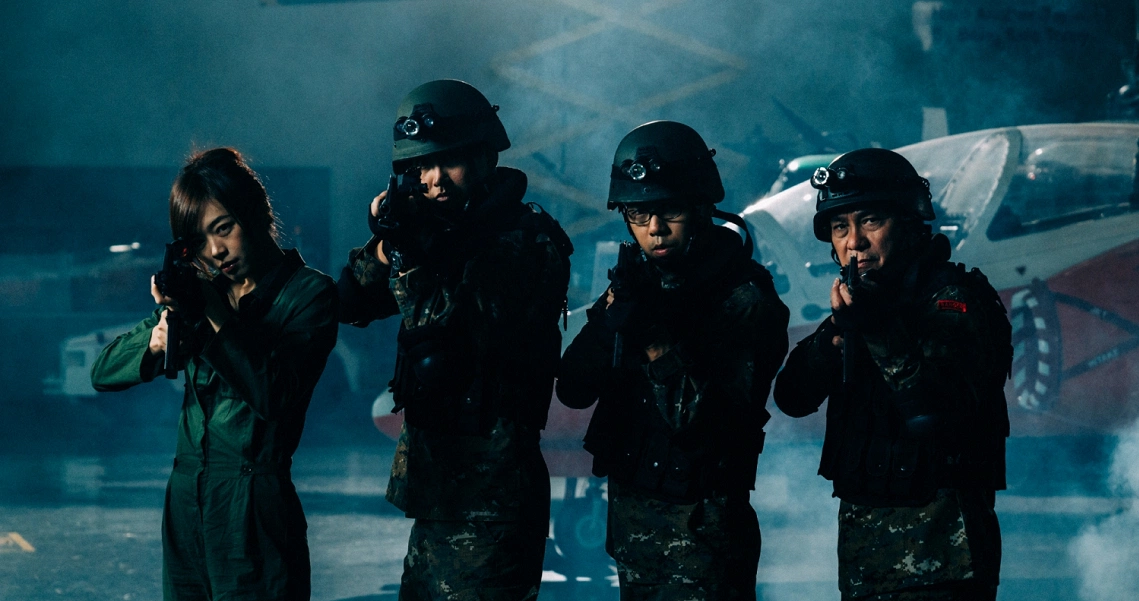 Zombiepura film still shows four armed soldiers in tactical gear, standing alert in a smoky, blue-tinted environment.