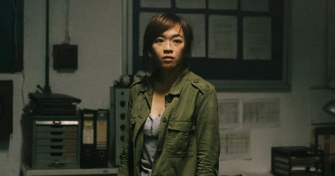 A woman in military uniform stands in a dimly lit room, looking concerned in this still from the Singaporean film Zombiepura.