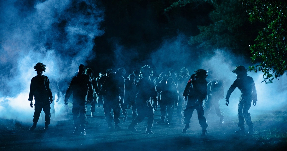 A scene from Zombiepura showing silhouettes of soldiers and zombies emerging from blue smoke in a dark, eerie atmosphere.