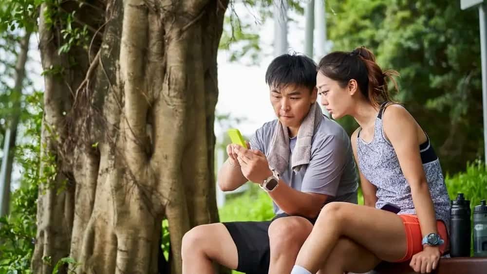Two people sitting on a bench at a park looking at a mobile phone